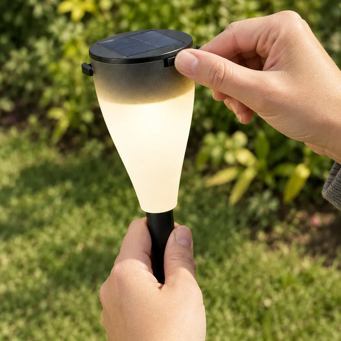 Mano sosteniendo una luz solar para camino con pantalla esmerilada encendida