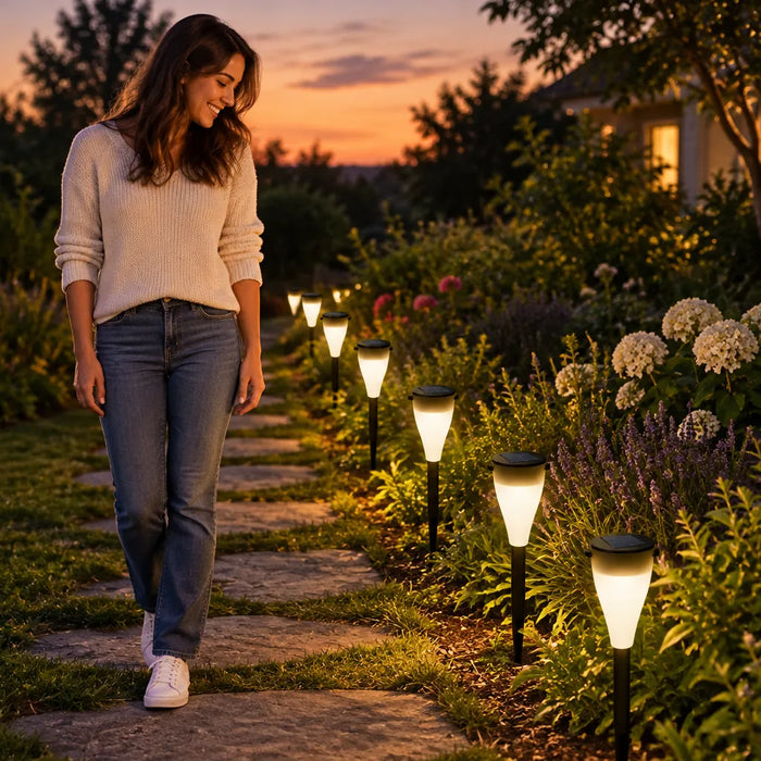 Mujer sonriendo junto a un camino de jardín iluminado con luces solares al atardecer