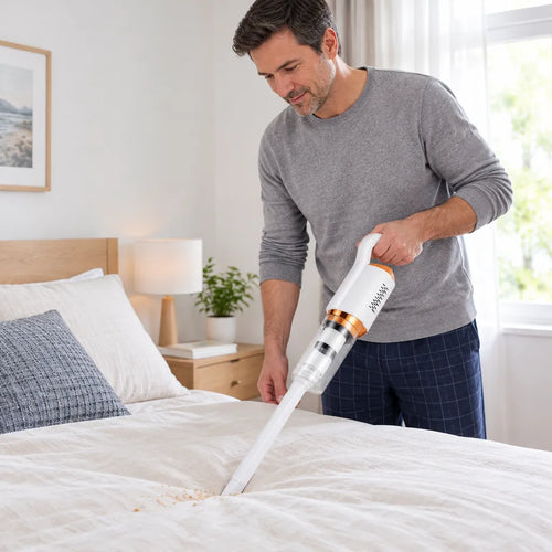 Mann reinigt mit einem kabellosen Handstaubsauger Krümel auf dem Bett