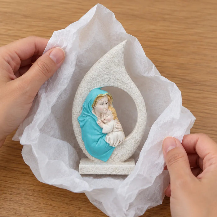 Hands unwrapping a Virgin Mary resin figurine from white tissue paper