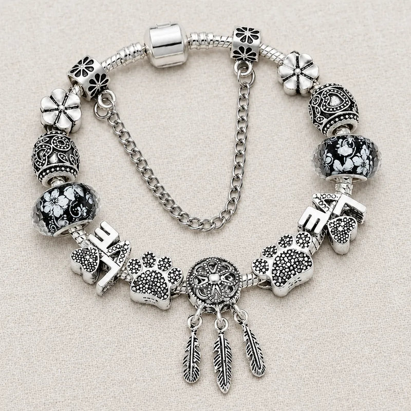 Pulsera plateada con atrapasueños, huellas y dijes LOVE sobre una superficie de lino