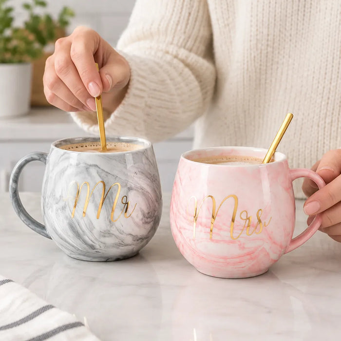 Hand stirring coffee with a gold spoon in a pink marble Mrs mug beside the grey Mr mug