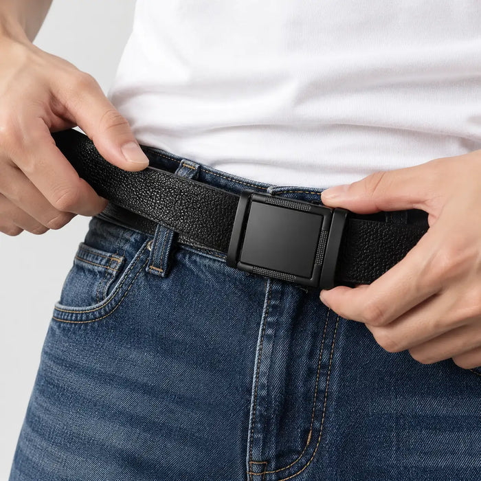 Hands sliding a black belt strap through a matte ratchet buckle on jeans