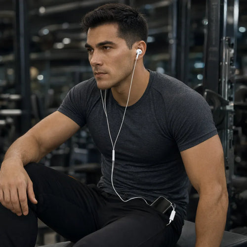 Hombre descansando en el gimnasio con audifonos con cable conectados al celular