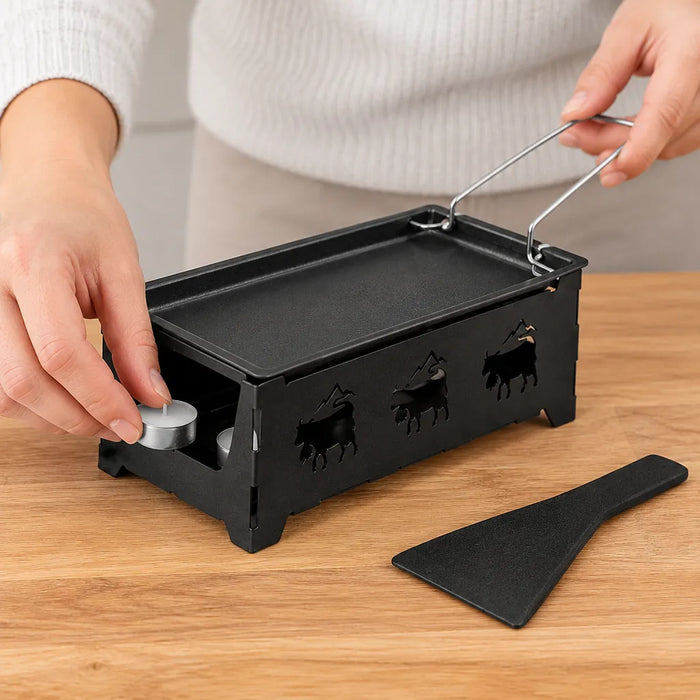 Hände stellen Teelichter in den schwarzen Rechaud eines Mini Raclette Ofens