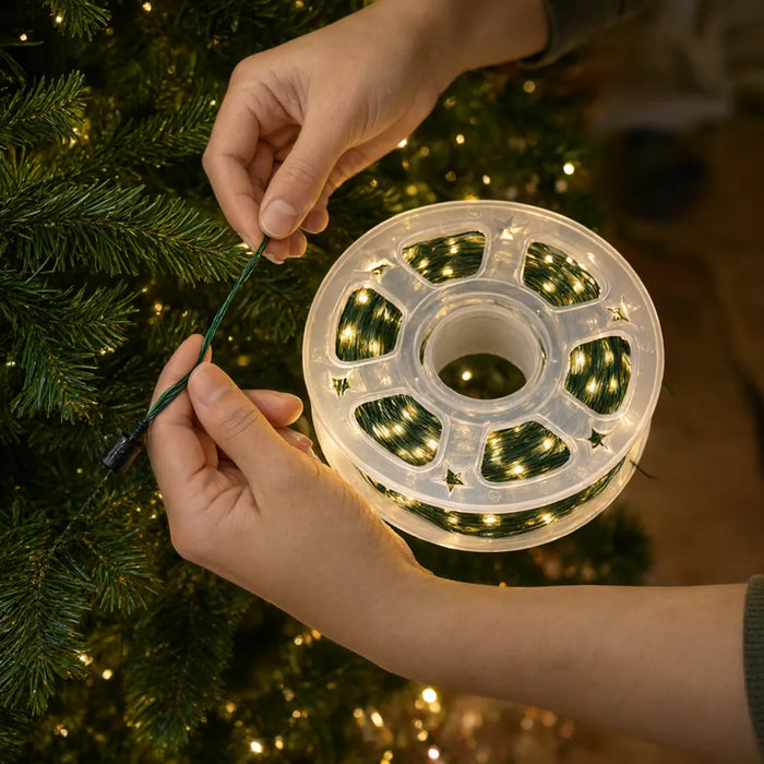 Hände rollen eine LED-Lichterkette für den Weihnachtsbaum von der Spule ab und wickeln den grünen Draht um den Baum