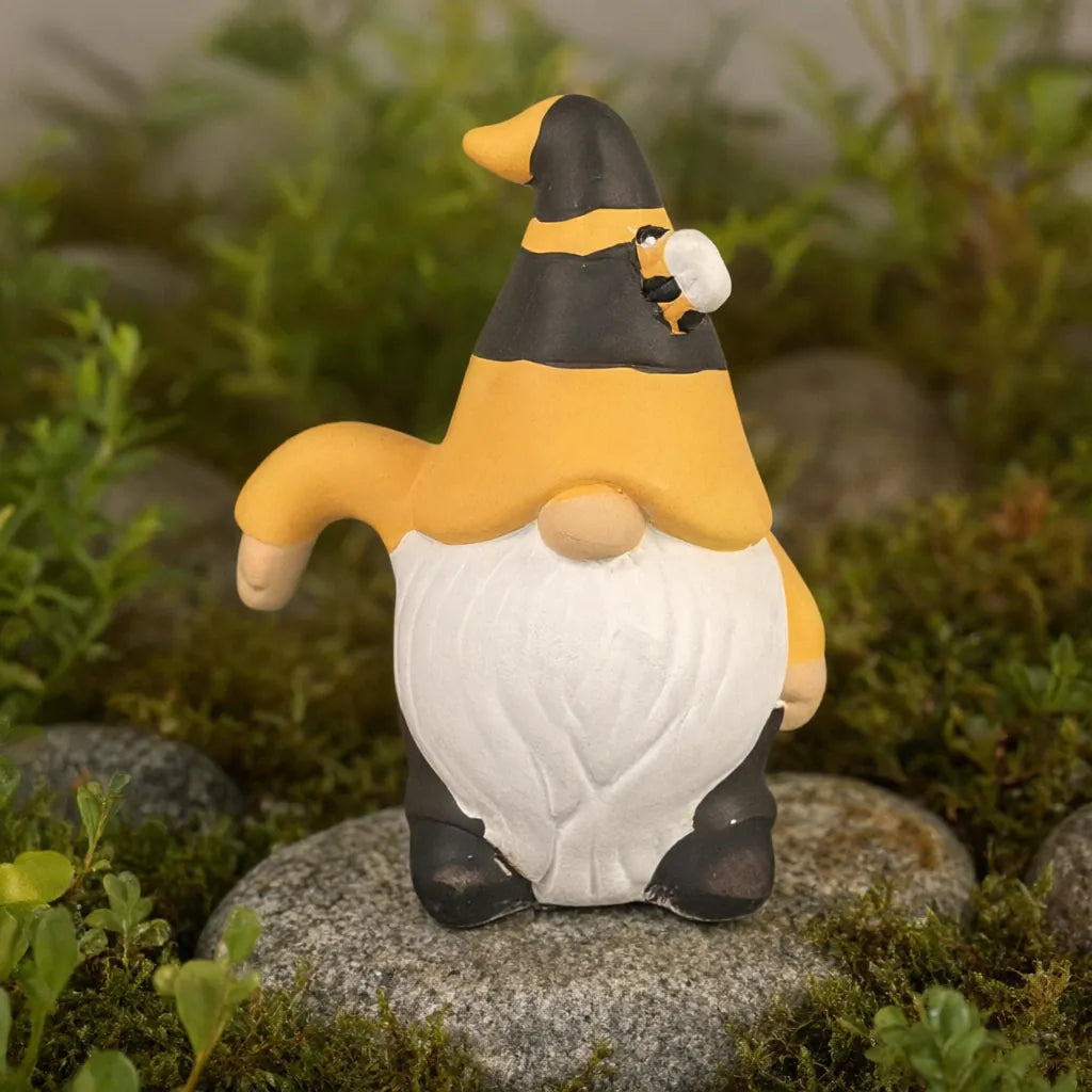 Small ceramic bee gnome standing on a stone among moss and plants