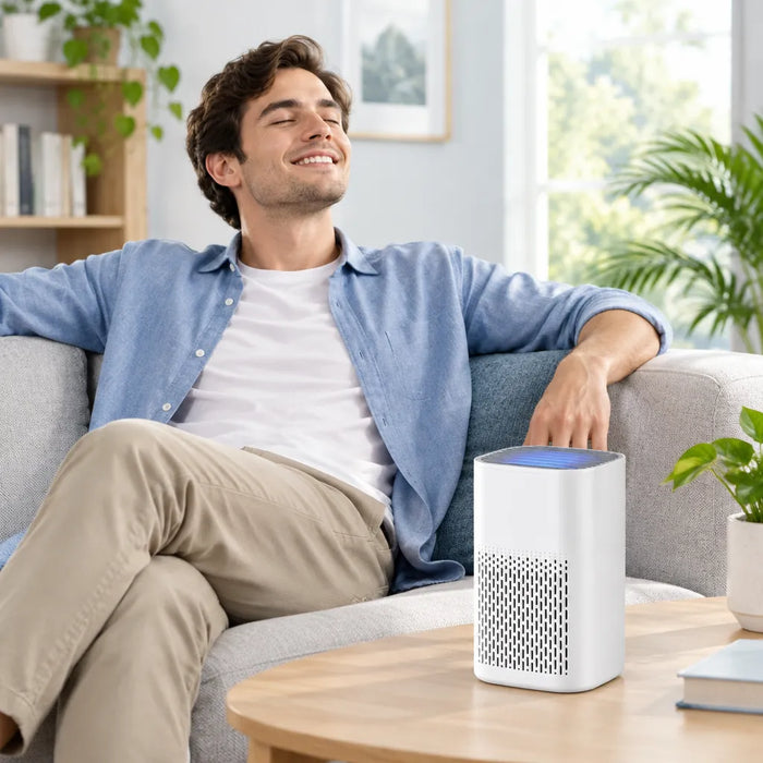 Smiling man relaxing on a sofa in a bright living room with a small HEPA air purifier on the coffee table