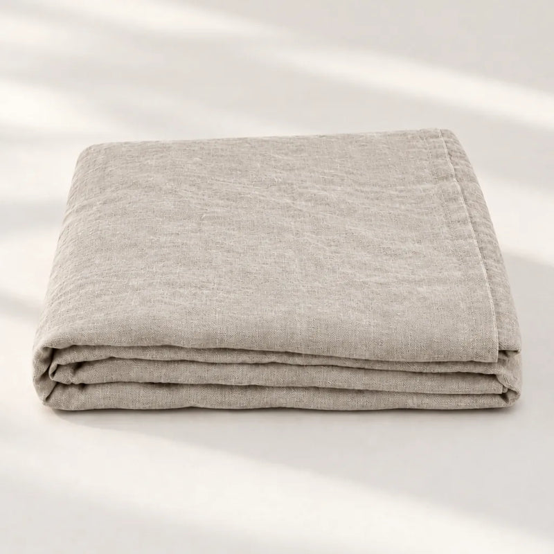 One folded natural linen flat bed sheet on a light surface