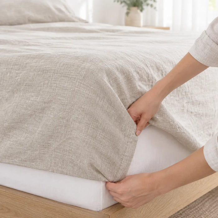 Hands tucking the corner of a linen bed sheet under the mattress