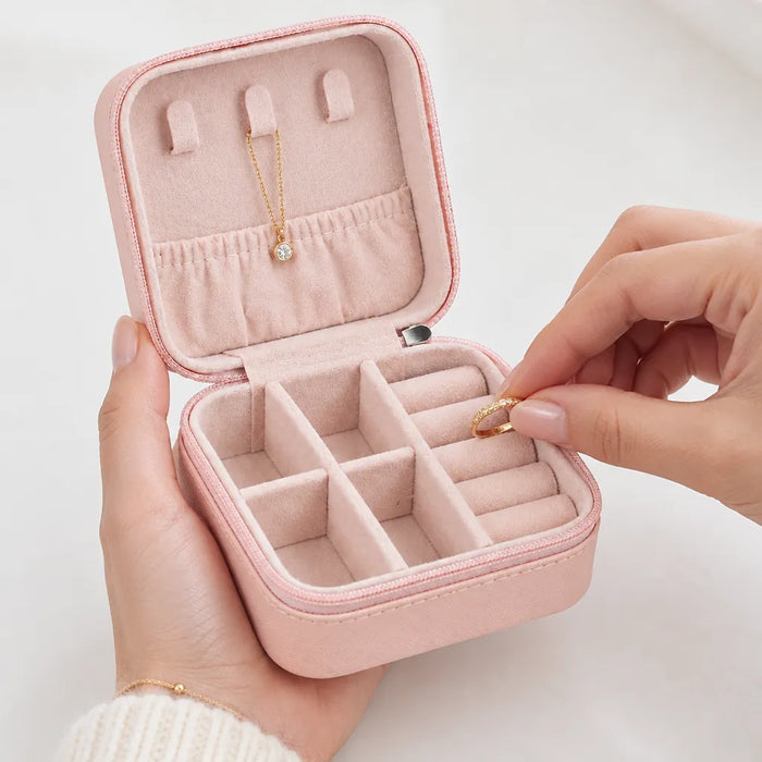 Mains qui rangent une bague dans une boîte à bijoux de voyage rose, un collier accroché au couvercle