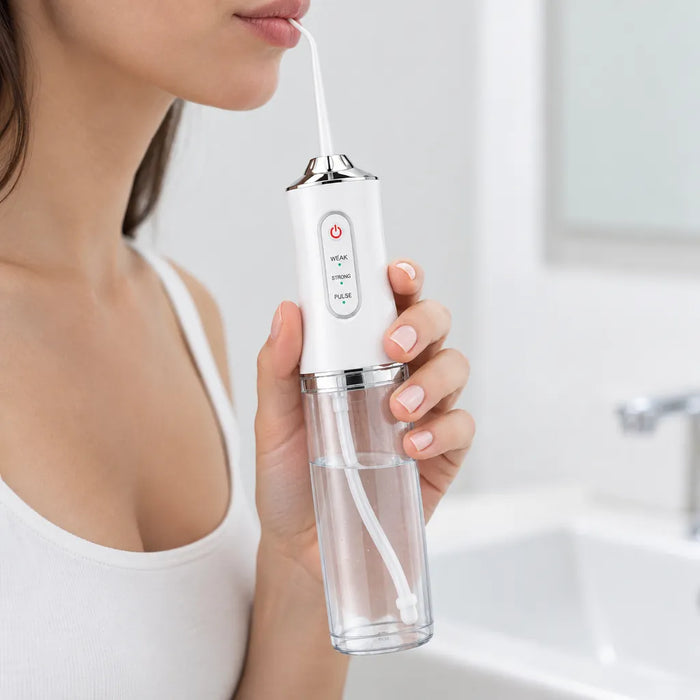 Woman holding a white cordless water flosser at her lips over a bathroom sink