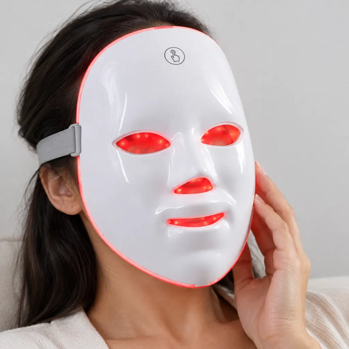 Woman relaxing with a white LED face mask glowing red over her face, head strap at the side
