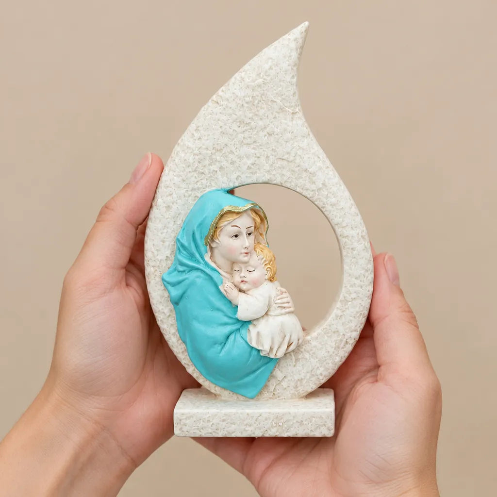 Hands holding a resin Virgin Mary statue with Baby Jesus in a teardrop frame
